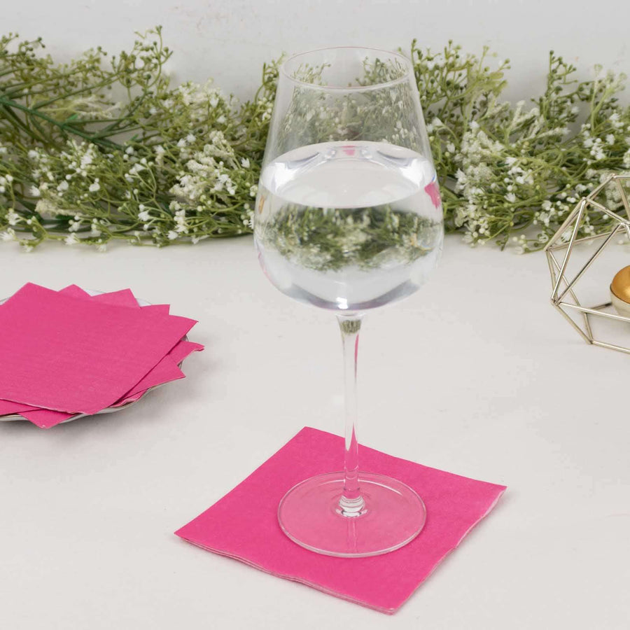 Clear wine glass filled with water on a pink napkin, surrounded by decorative greenery.