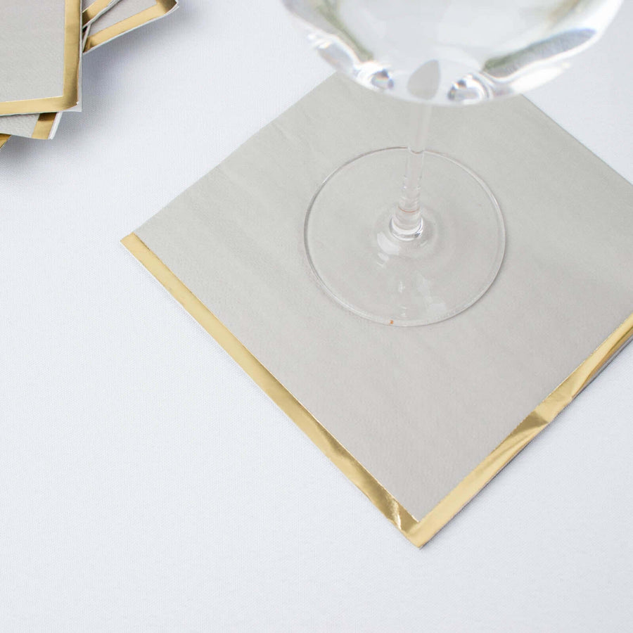 Elegant gray napkin with gold trim under a glass on a plain background.
