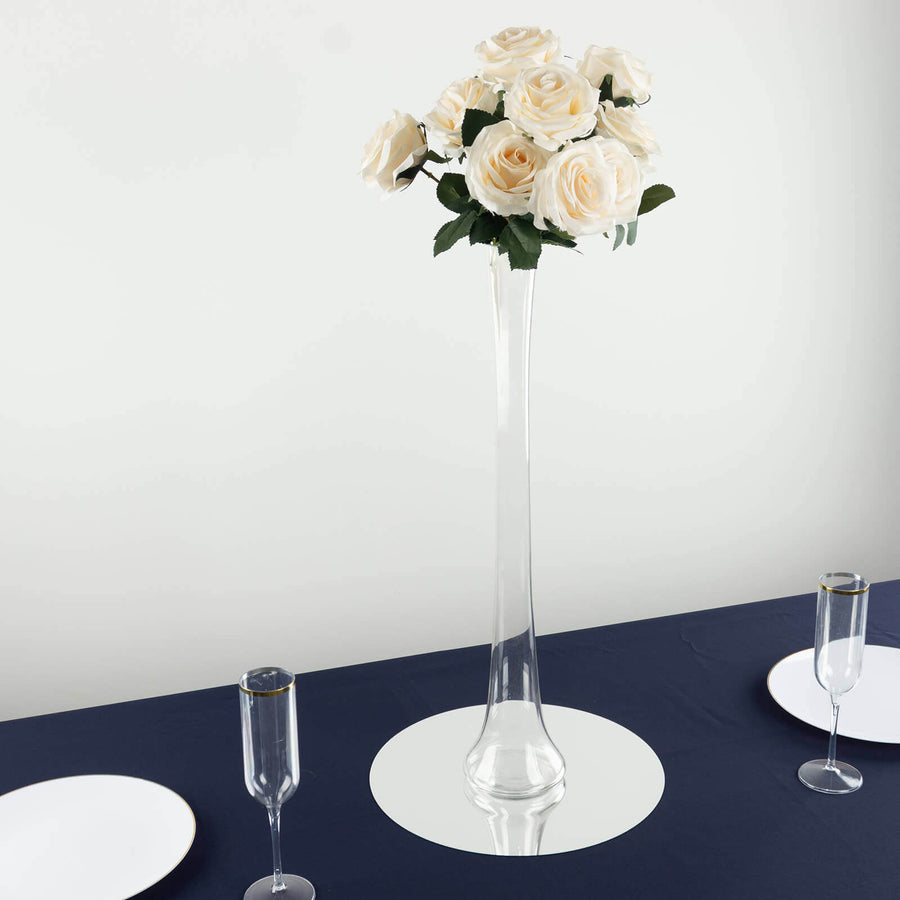 Tall glass vase with white rose bouquet on a dining table setting.