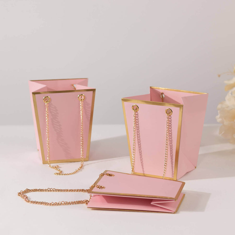 Pink gift bags with gold accents and chains on a plain background.