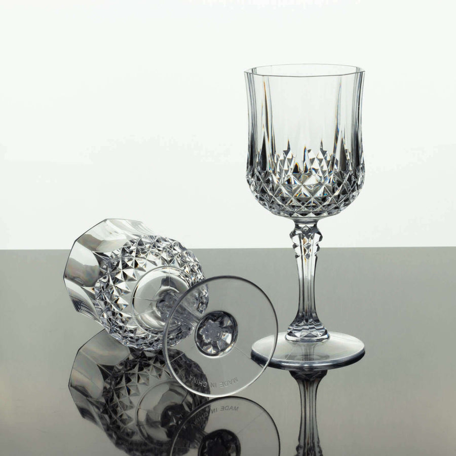 Crystal wine glasses on a reflective surface, one upright and one toppled.