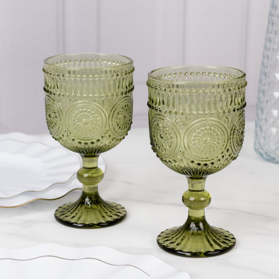 Green decorative goblets on a marble table with white plates in the background.