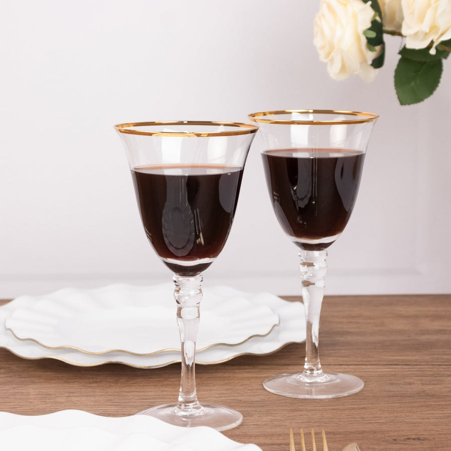 Elegant crystal wine glasses with gold rims filled with red wine.