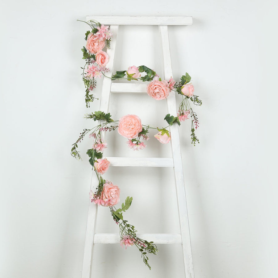 Floral garland with pink roses and greenery draped over a white ladder.