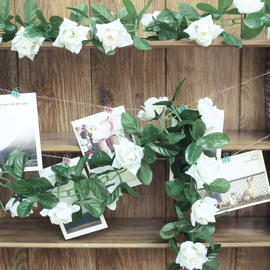 Artificial white roses and photos hanging on a wooden shelf.