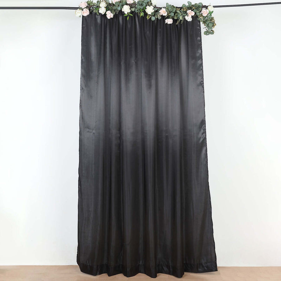 Black satin curtain with floral accents hanging in a studio setting.