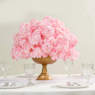 Pink hydrangea floral centerpiece in a gold vase on a dining table.
