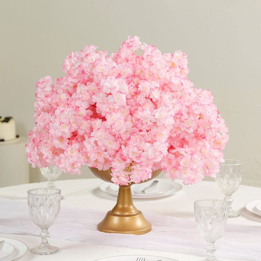 Pink floral centerpiece in a gold vase on a dining table.