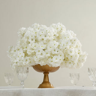White floral arrangement in a gold vase with crystal glasses.
