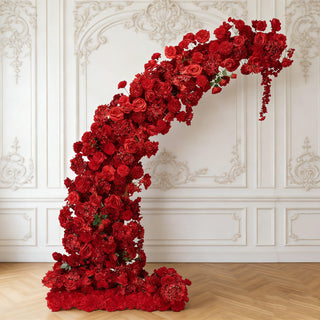 Red floral installation arch with roses and blooms against a decorative wall.