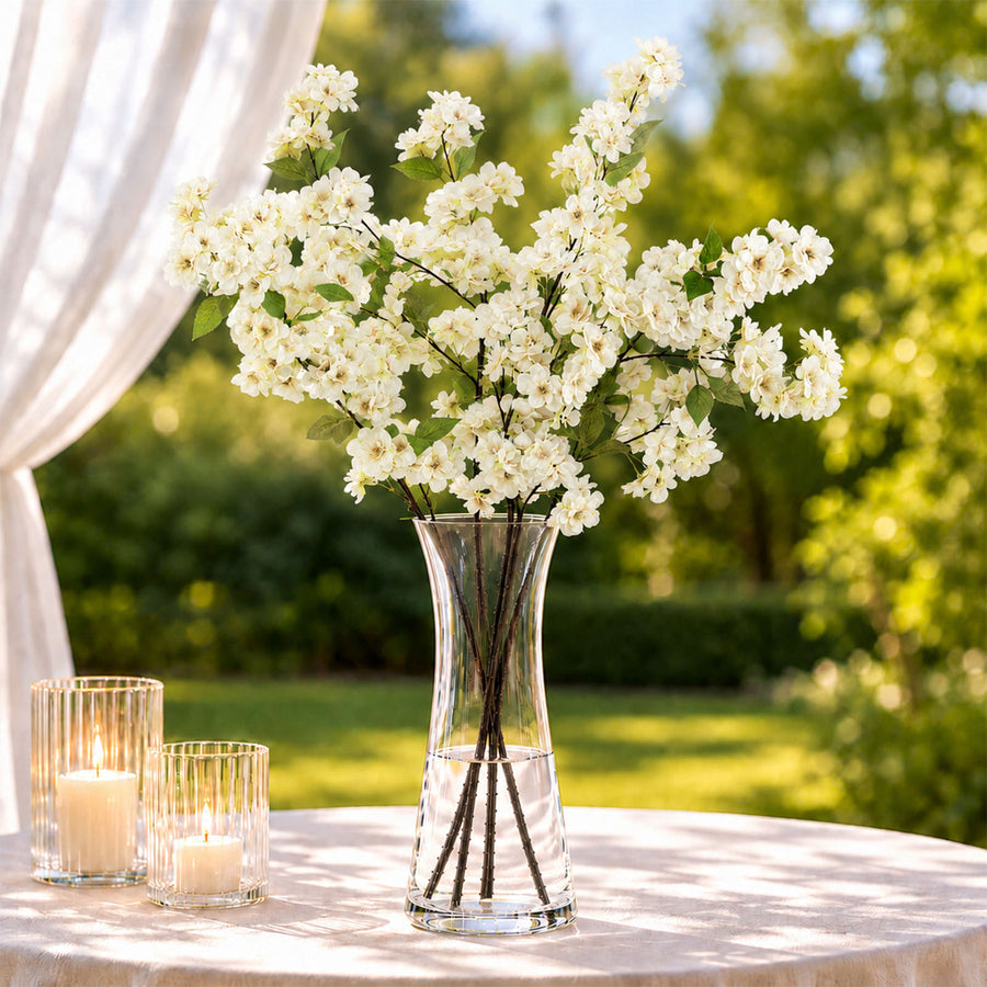 Elegant white floral centerpiece in glass vase with candles on outdoor table