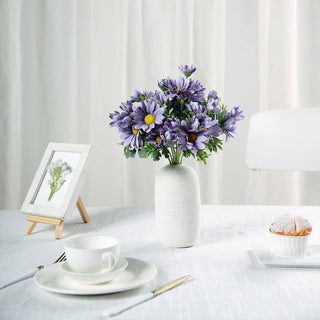 Purple flower bouquet in a vase on a dining table with tea set and framed picture.