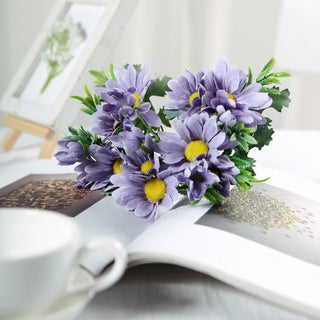 Purple artificial flowers arrangement on a magazine with a coffee cup.