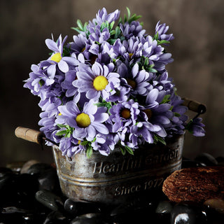 Purple daisies in a rustic metal bucket on a decorative surface.