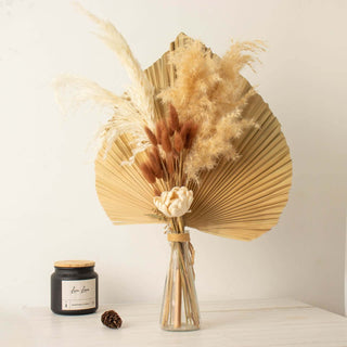 Dried flower bouquet in a glass vase with decorative fan leaves.