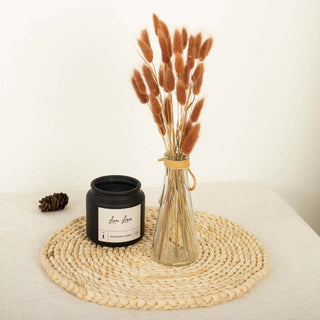 Black candle and glass vase with dried flowers on a woven placemat.