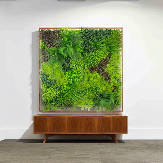 Artificial green wall art in a wooden frame above a modern sideboard.