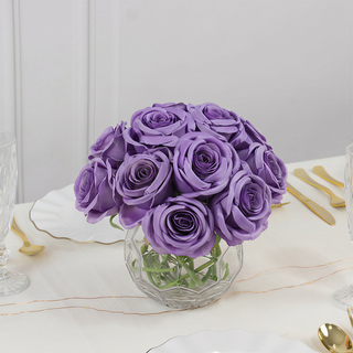 Purple rose bouquet in a clear vase on a table setting.