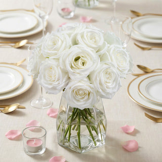 White rose bouquet in a glass vase on a dining table with elegant tableware.