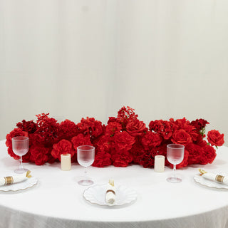 Red floral table centerpiece with glasses and candles on a white table.