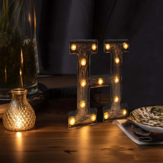 Decorative light-up letter "H" with warm bulbs on a wooden table.