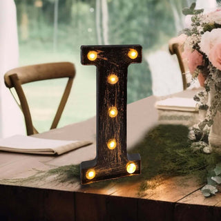 Decorative illuminated letter "I" on a rustic table with flowers.