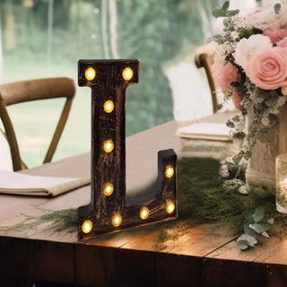 Rustic marquee letter "L" with lights on a table decorated with flowers.