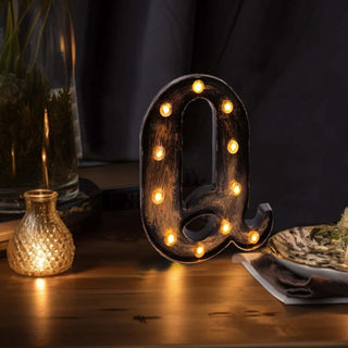 Decorative vintage marquee letter "Q" with lights on a wooden table.