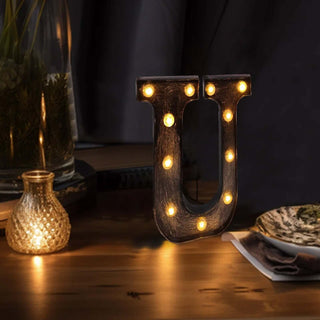 Illuminated marquee letter "U" on a wooden table with soft lighting.