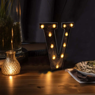 Decorative marquee letter "V" with warm lights on a rustic table setting.
