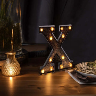 Illuminated decorative letter "X" with vintage bulbs on a table setting.
