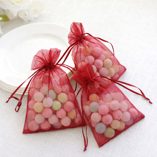 Red organza bags filled with colorful candies on a white tablecloth.