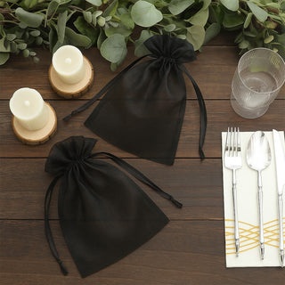 Black organza gift bags on a wooden table with candles and tableware.