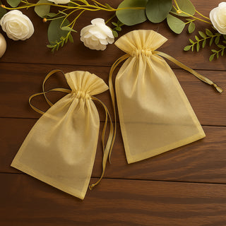 Two yellow organza gift bags on a wooden surface surrounded by greenery.