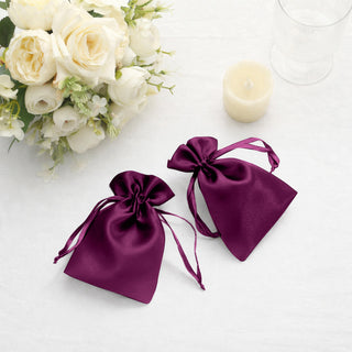 Purple satin drawstring bags on a table with flowers and candle.