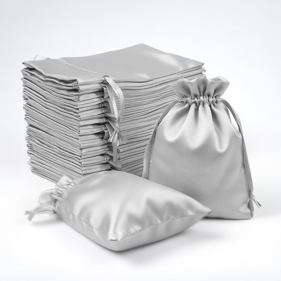 Silver satin drawstring bags stacked and arranged on a white backdrop.