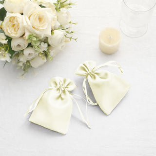 Elegant pale yellow satin bags beside a bouquet of white roses and a candle.