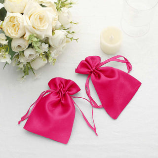 Two pink satin gift bags with drawstrings on a table with flowers.