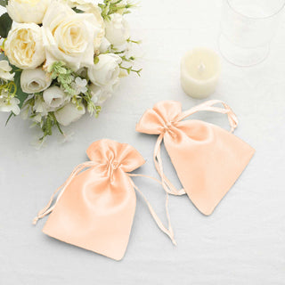 Peach satin drawstring bags on a table with white flowers and a candle.