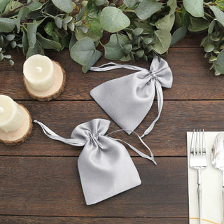 Elegant gray satin favor bags on a rustic wooden table with candles and greenery.
