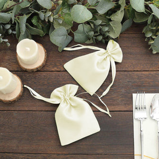 Satin favor bags with bows on a wooden table with greenery and candles.