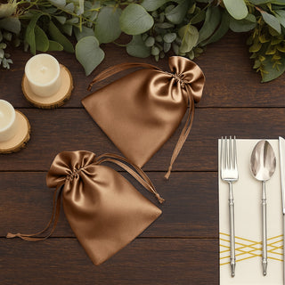 Brown satin gift bags on a wooden table with candles and cutlery.