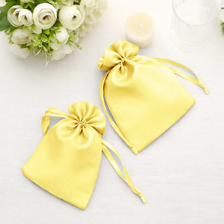Yellow satin drawstring bags on a table with flowers and a candle.