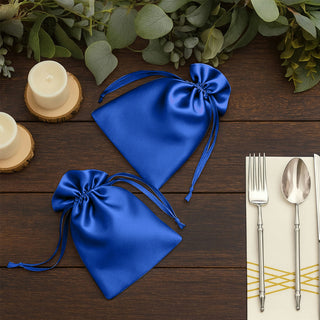 Blue satin drawstring bags on a wooden table with candles and utensils.