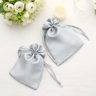Two silver satin drawstring bags on a soft white surface.