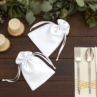 White satin drawstring bags on a wooden table with candles and utensils.