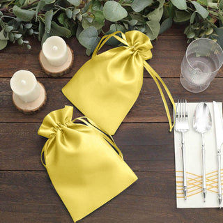 Yellow satin gift bags on a rustic table with candles and cutlery.