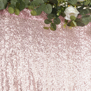 Rose gold sequin backdrop with greenery and white flowers.