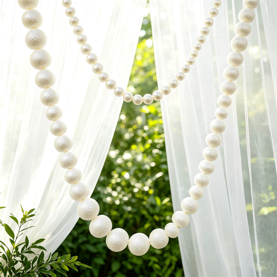 White pearl garland draped between sheer curtains in a garden setting