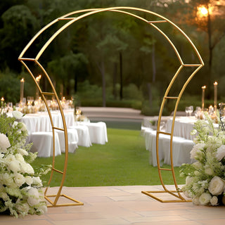 Elegant gold wedding arch surrounded by white floral arrangements in a garden setting.